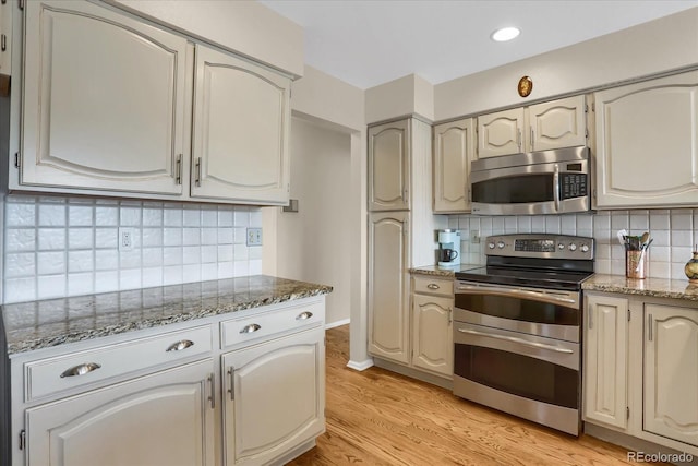 kitchen featuring stainless steel appliances, light hardwood / wood-style floors, stone counters, and decorative backsplash