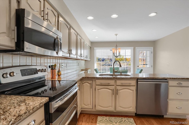 kitchen with light hardwood / wood-style floors, sink, backsplash, appliances with stainless steel finishes, and decorative light fixtures