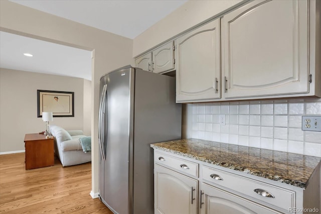 kitchen with light hardwood / wood-style floors, tasteful backsplash, white cabinetry, dark stone countertops, and stainless steel fridge