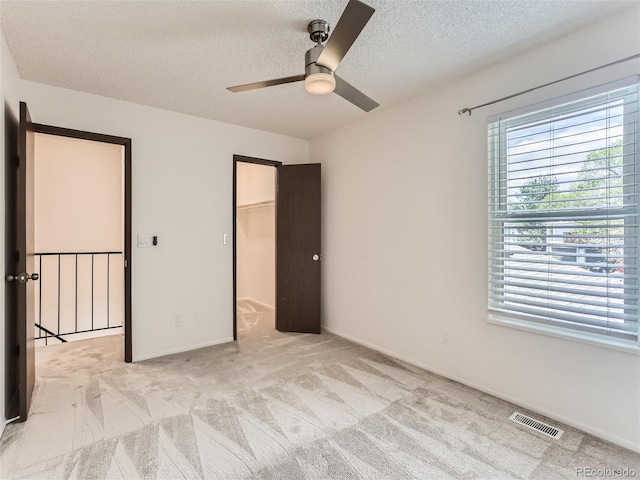 unfurnished bedroom featuring a closet, a textured ceiling, light carpet, a spacious closet, and ceiling fan