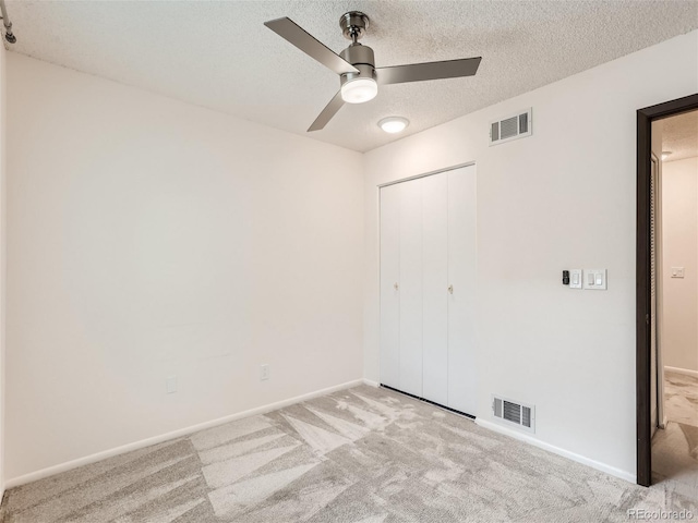 unfurnished bedroom featuring a closet, ceiling fan, light colored carpet, and a textured ceiling