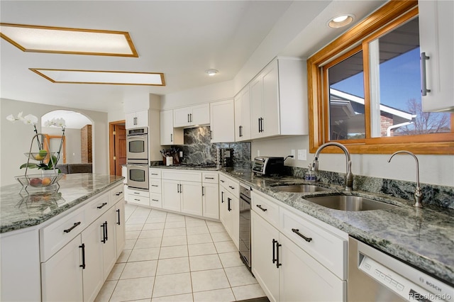 kitchen with a sink, backsplash, white cabinetry, appliances with stainless steel finishes, and light tile patterned flooring