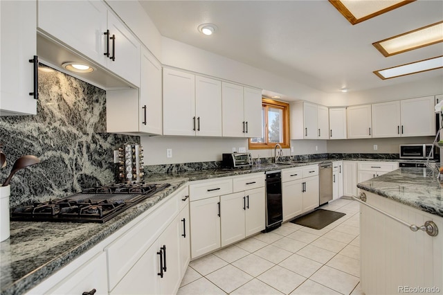 kitchen featuring light tile patterned floors, dark stone counters, white cabinetry, stainless steel microwave, and black gas stovetop