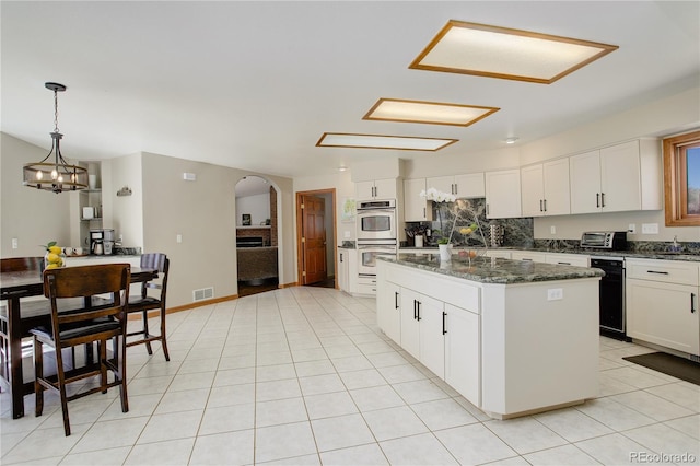 kitchen with a center island, white cabinetry, stainless steel double oven, arched walkways, and light tile patterned flooring