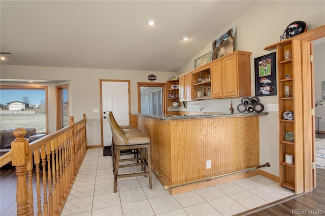 kitchen featuring lofted ceiling, open shelves, light tile patterned floors, and stone counters