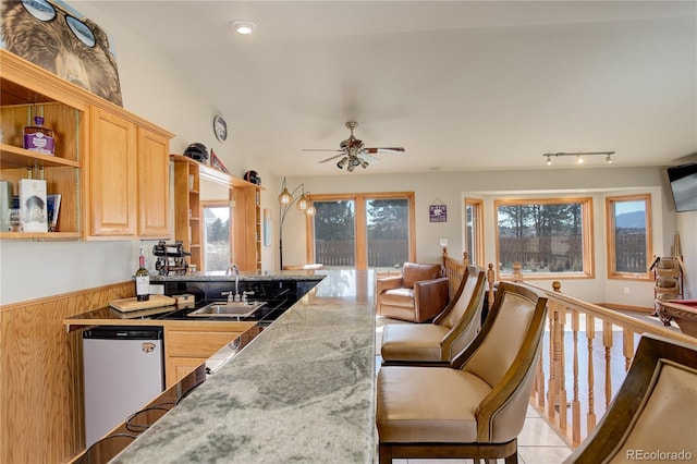 kitchen featuring a ceiling fan, light brown cabinets, a peninsula, a sink, and a kitchen breakfast bar