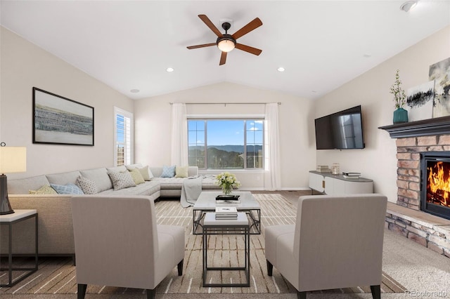 living room with ceiling fan, a stone fireplace, carpet floors, and vaulted ceiling