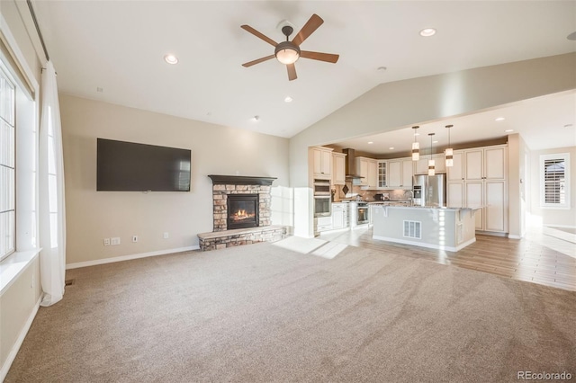 unfurnished living room with a stone fireplace, ceiling fan, light colored carpet, and lofted ceiling