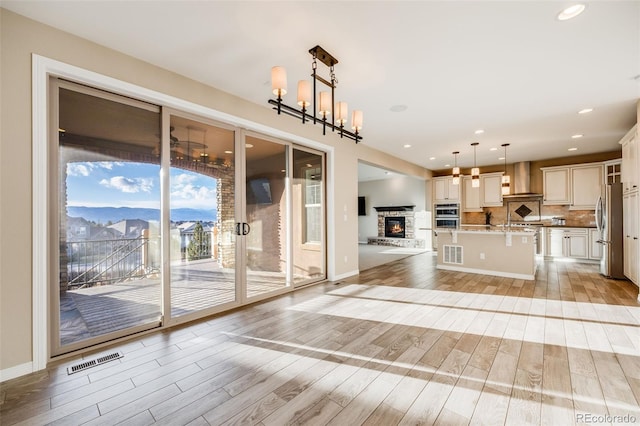 kitchen with stainless steel appliances, hanging light fixtures, a kitchen breakfast bar, light hardwood / wood-style floors, and a kitchen island with sink