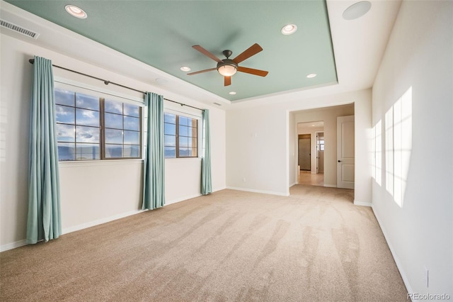 unfurnished room with a tray ceiling, ceiling fan, and light carpet