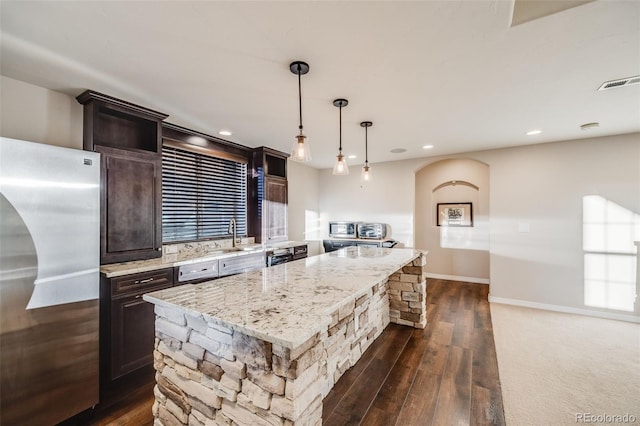 kitchen with stainless steel refrigerator, light stone counters, dark hardwood / wood-style flooring, pendant lighting, and a kitchen island