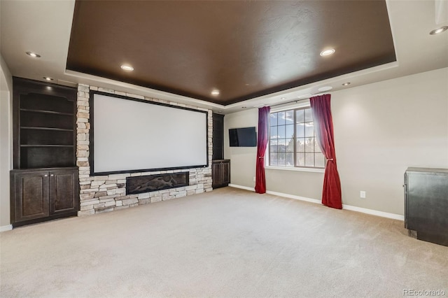 cinema room with a large fireplace, light carpet, and a tray ceiling