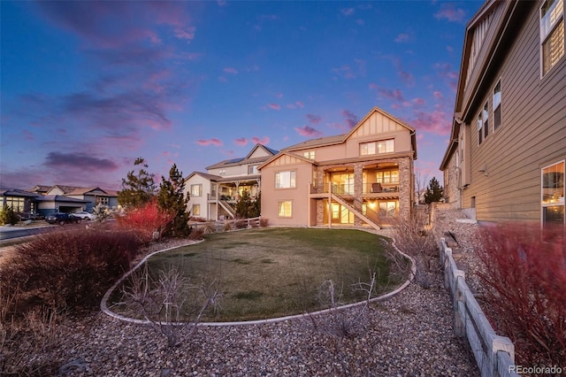 back house at dusk featuring a yard and a balcony