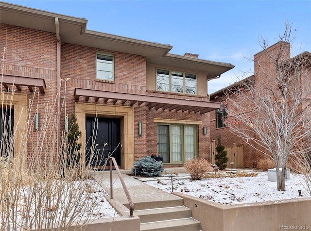 snow covered back of property featuring brick siding