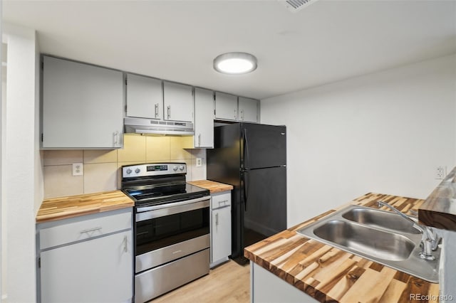kitchen with electric stove, butcher block countertops, freestanding refrigerator, under cabinet range hood, and a sink