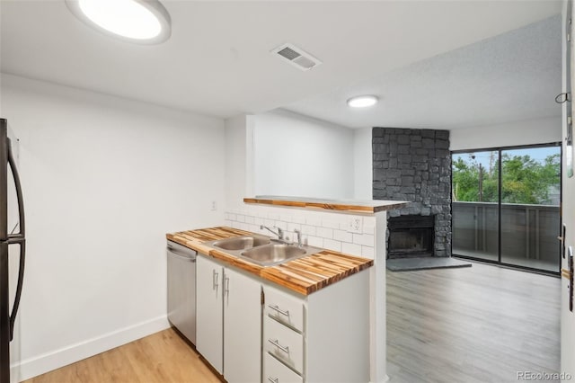 kitchen with a sink, wood counters, dishwasher, light wood-style floors, and tasteful backsplash