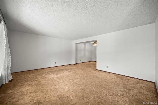carpeted spare room featuring a textured ceiling, a ceiling fan, and baseboards