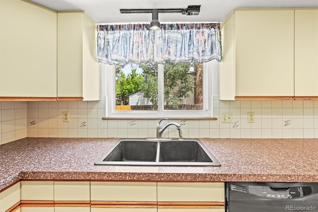 kitchen featuring a sink, black dishwasher, cream cabinets, decorative backsplash, and dark countertops
