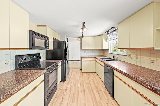 kitchen featuring black appliances, a sink, light wood-style floors, and dark countertops