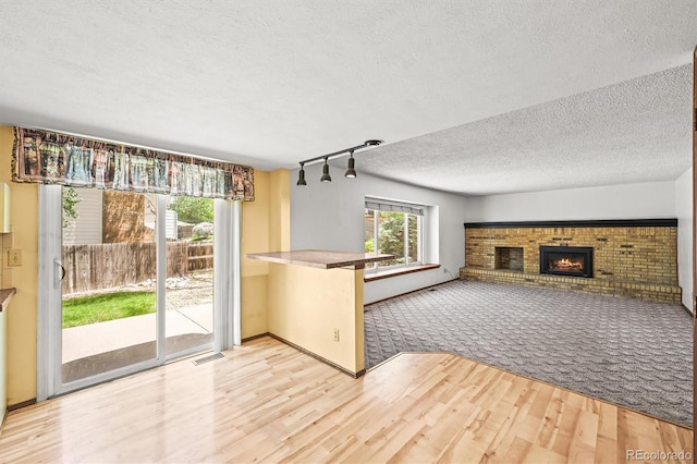 unfurnished living room with wood finished floors, a textured ceiling, a brick fireplace, rail lighting, and carpet