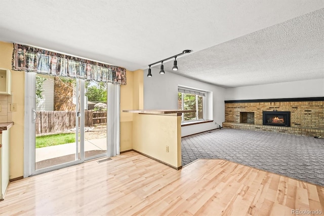unfurnished living room with a fireplace, wood finished floors, a textured ceiling, track lighting, and baseboards