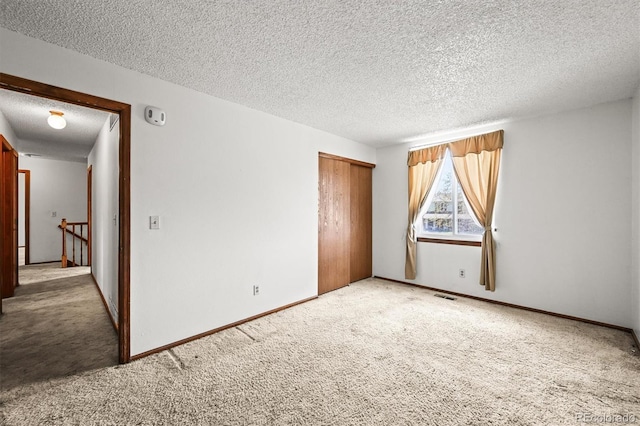 empty room featuring a textured ceiling, light carpet, and baseboards