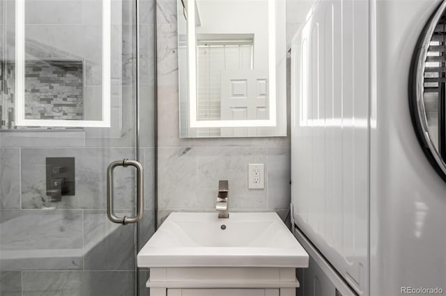 bathroom with a shower with door, washer / clothes dryer, decorative backsplash, and vanity