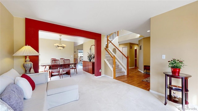 carpeted living room featuring a chandelier, stairway, and baseboards