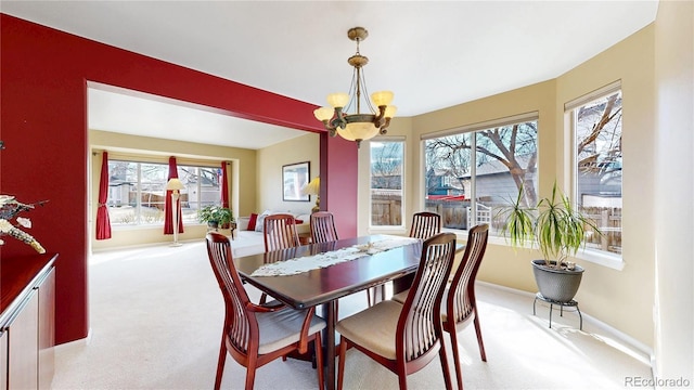 dining space featuring light carpet, baseboards, and an inviting chandelier