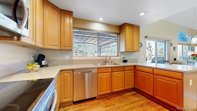 kitchen featuring stainless steel appliances, a peninsula, a sink, light countertops, and light wood finished floors