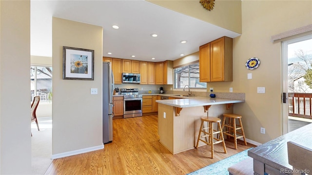 kitchen featuring a peninsula, stainless steel appliances, a sink, a kitchen breakfast bar, and light countertops