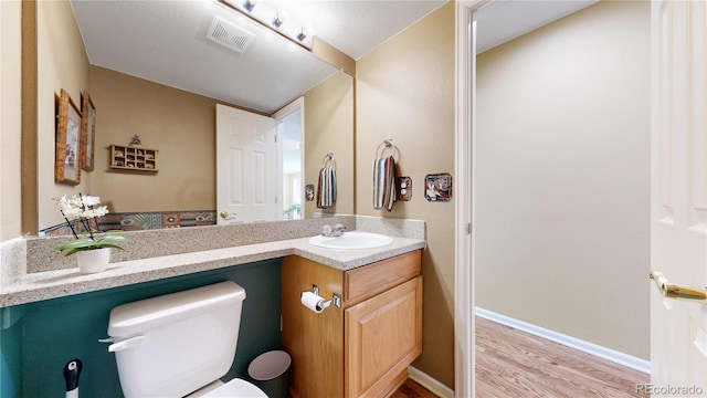 bathroom featuring baseboards, visible vents, toilet, wood finished floors, and vanity