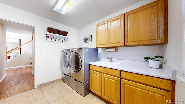 washroom with light tile patterned floors, a sink, baseboards, washer and dryer, and cabinet space