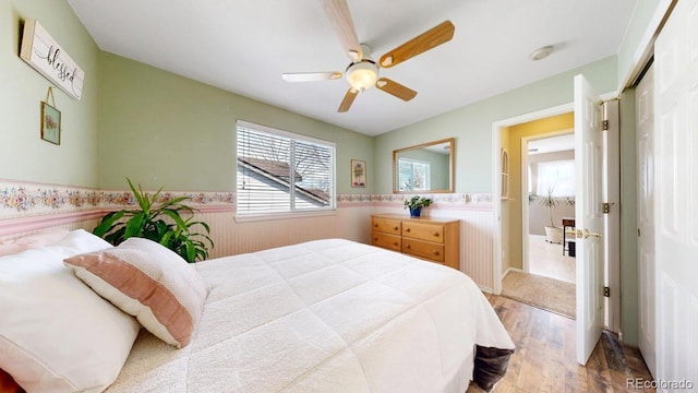 bedroom featuring a ceiling fan, a closet, wainscoting, and wood finished floors