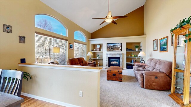 living area featuring built in features, a tiled fireplace, ceiling fan, high vaulted ceiling, and baseboards