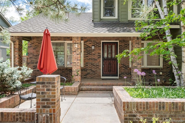 entrance to property featuring brick siding and a shingled roof