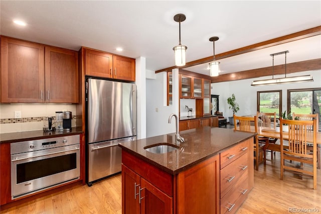 kitchen with stainless steel appliances, a sink, light wood-type flooring, dark stone countertops, and brown cabinetry
