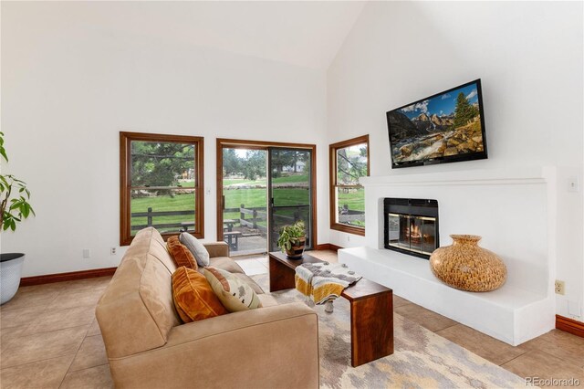 living room featuring tile patterned floors, high vaulted ceiling, a glass covered fireplace, and baseboards