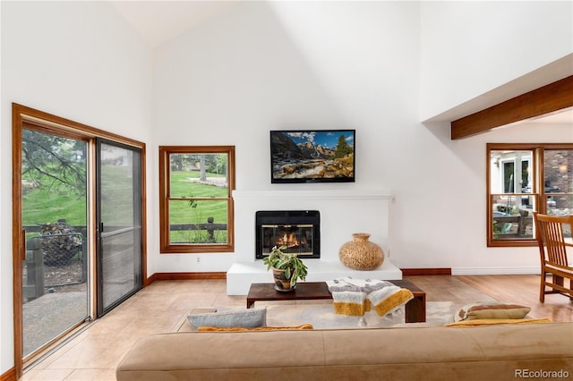 living area with high vaulted ceiling, a glass covered fireplace, and baseboards