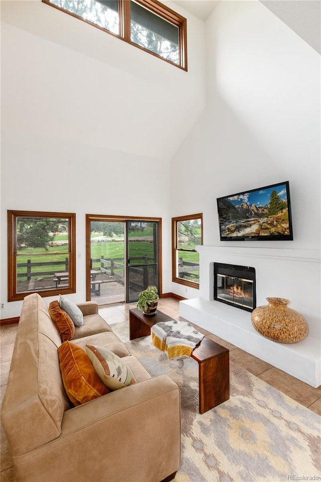 tiled living area featuring high vaulted ceiling, a glass covered fireplace, and baseboards