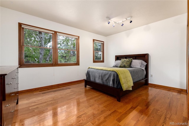 bedroom featuring baseboards, track lighting, and light wood finished floors