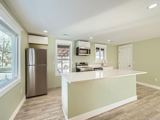 kitchen featuring white cabinets, a center island, light wood-type flooring, and appliances with stainless steel finishes