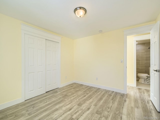 unfurnished bedroom featuring a closet, ensuite bathroom, and light hardwood / wood-style flooring