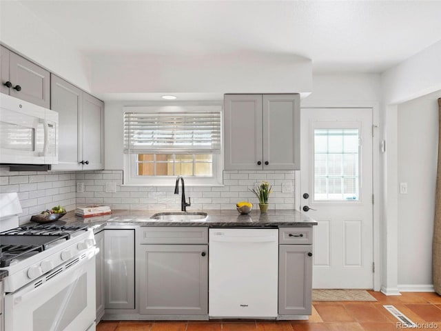 kitchen with decorative backsplash, sink, light tile patterned floors, white appliances, and dark stone countertops