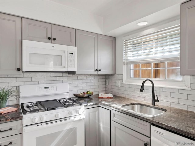 kitchen featuring tasteful backsplash, sink, gray cabinetry, white appliances, and dark stone countertops