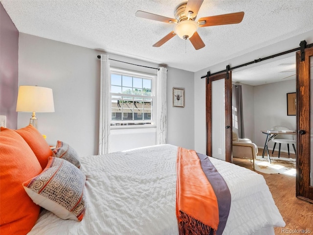 bedroom featuring hardwood / wood-style flooring, a textured ceiling, a barn door, and ceiling fan