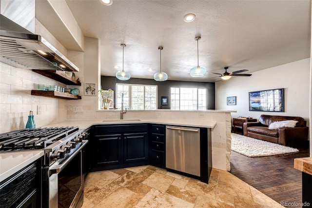 kitchen featuring wall chimney range hood, sink, kitchen peninsula, pendant lighting, and stainless steel appliances