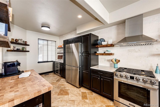 kitchen with wall chimney exhaust hood, backsplash, stainless steel appliances, butcher block countertops, and dark brown cabinetry