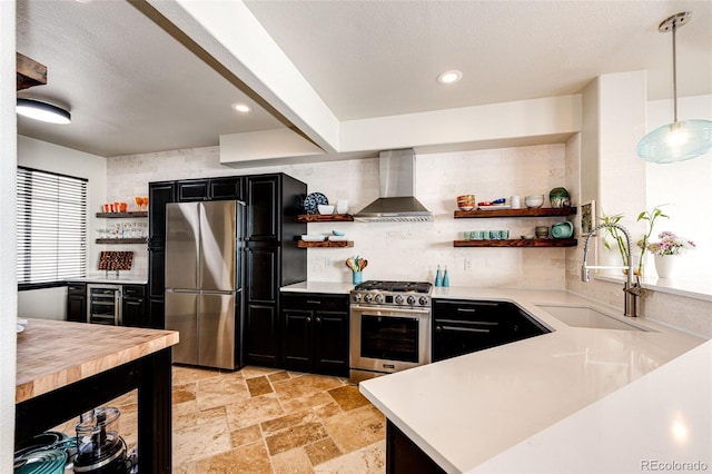 kitchen featuring wall chimney range hood, decorative light fixtures, kitchen peninsula, stainless steel appliances, and wine cooler