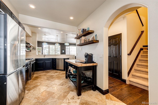 kitchen with butcher block counters, appliances with stainless steel finishes, hanging light fixtures, sink, and kitchen peninsula